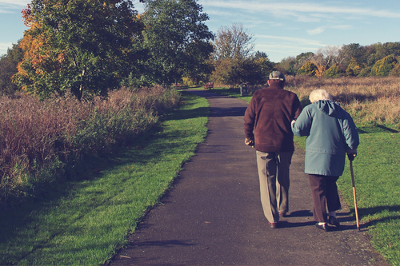 50 Days Older lady and gentleman walking on a path with walking aid