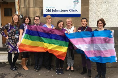 staff standing outside Old Johnstone Clinic holding a LGBT flag and a transgender pride flag